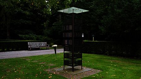 In het midden van een gazon staat een zuil met plaquettes erop.